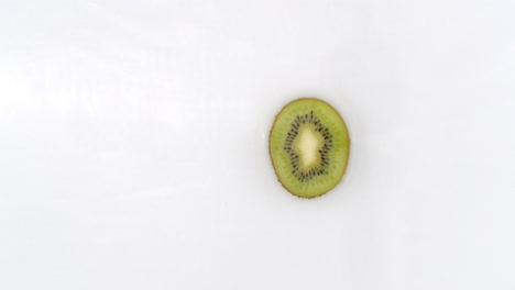 Slow-motion-water-splash-on-one-slice-of-kiwi-lying-on-a-white-background-in-water